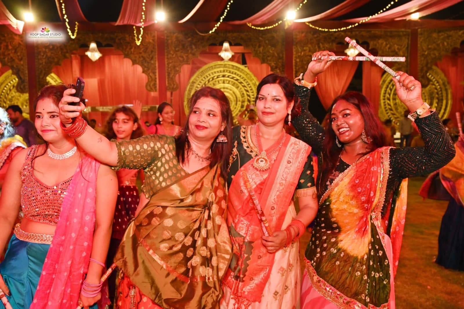 A couple posing with dandiya sticks beneath festive lights at Adarsh Vatika