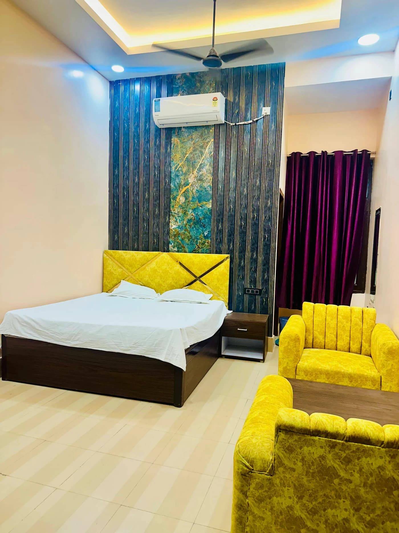 Portrait view of an Adarsh Vatika guest room with a double bed, air conditioning and lounge seating